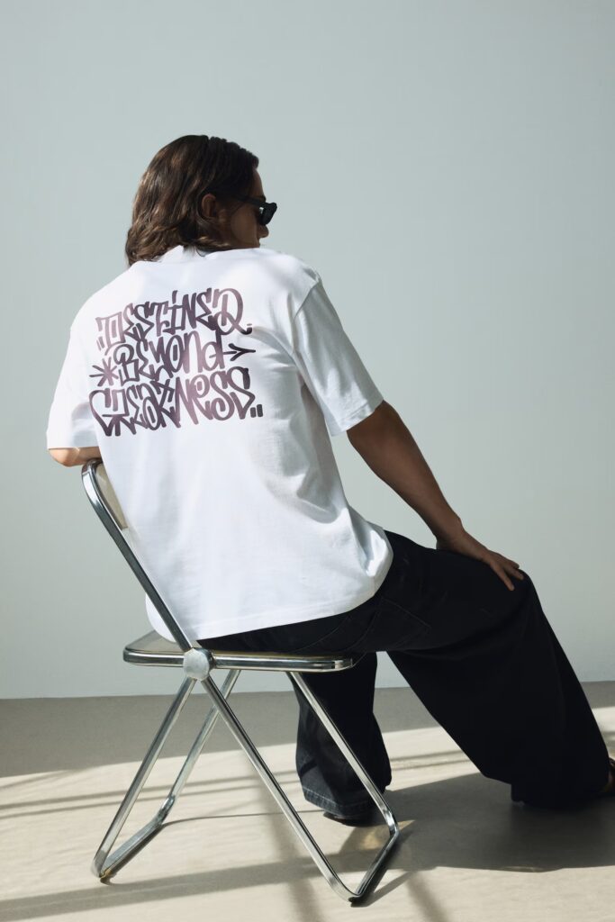 Man wearing the best t-shirt for men, white graphic tee, seated on a chair.
